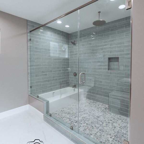 Modern bathroom with glass shower enclosure, gray tiles, and white bathtub.