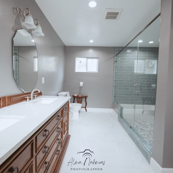 Modern bathroom with double vanity, large mirror, toilet, and glass shower.