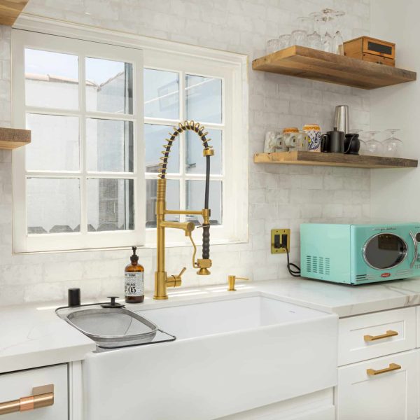 Modern kitchen with white farmhouse sink, gold faucet, and light blue microwave.