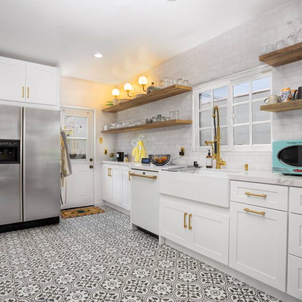Well-lit kitchen with white cabinets, stainless steel refrigerator, and patterned floor.