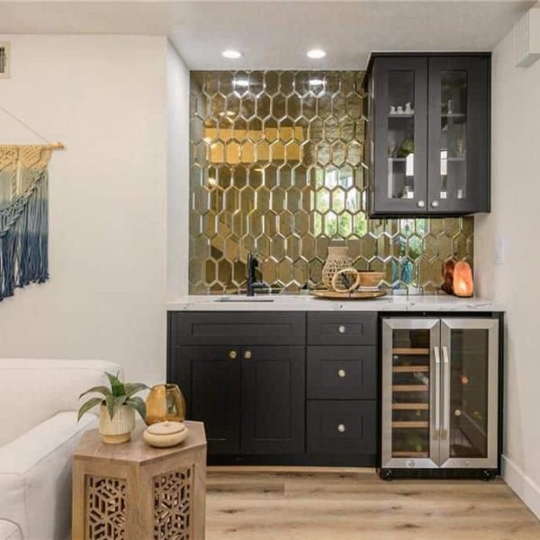 A modern home bar with gold hexagonal tiles and dark cabinetry.